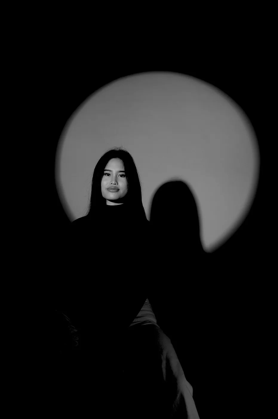Romana Ta in a dark room, lit by a round spotlight on the wall behind her